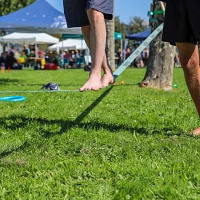 Eine Person balanciert auf einer Slackline, eine Person unterstützt. Zu sehen sind nur die Füße.