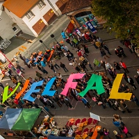 Aufnahme vom Dach in der Schulstraße: Straßenfest. Menschen halten große bunte Buchstaben in den Händen: das Wort ergibt 