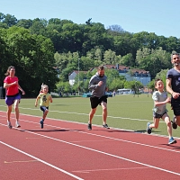 Eine Frau, zwei Männer und zwei Kinder laufen auf einer Laufbahn und lachen fröhlich.