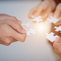 Nahaufnahme mehrerer Hände. Jede Hand hält ein Puzzleteil.