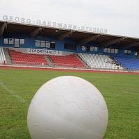 Blick auf die Tribüne des Georg-Gaßmann-Stadions, im Vordergrund liegt ein Ball auf dem Rasen.