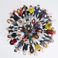 Luftaufnahme einer Gruppe von fröhlichen Menschen im Kreis. Sie heben die Hände und schauen in die Kamera.